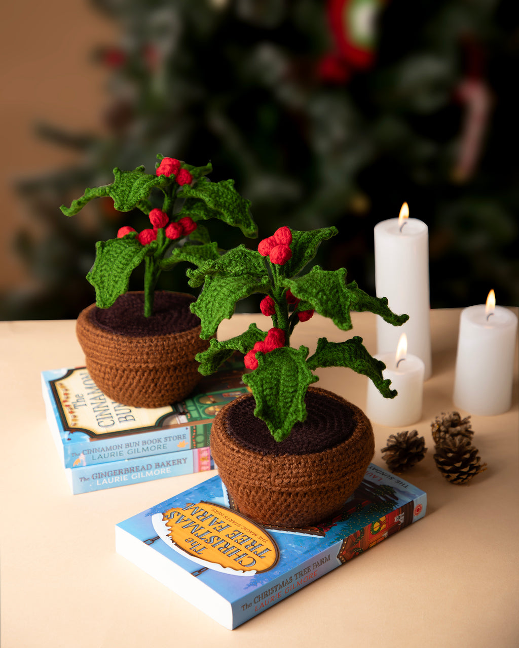 Crocheted plants in pots on books with candles and pinecones in the background